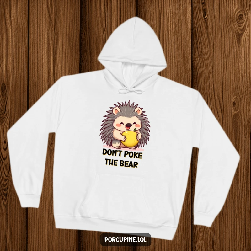 Funny hoodie featuring a wide-smiling porcupine comically attempting to balance a small fruit atop its quills, exuding joyful struggle.